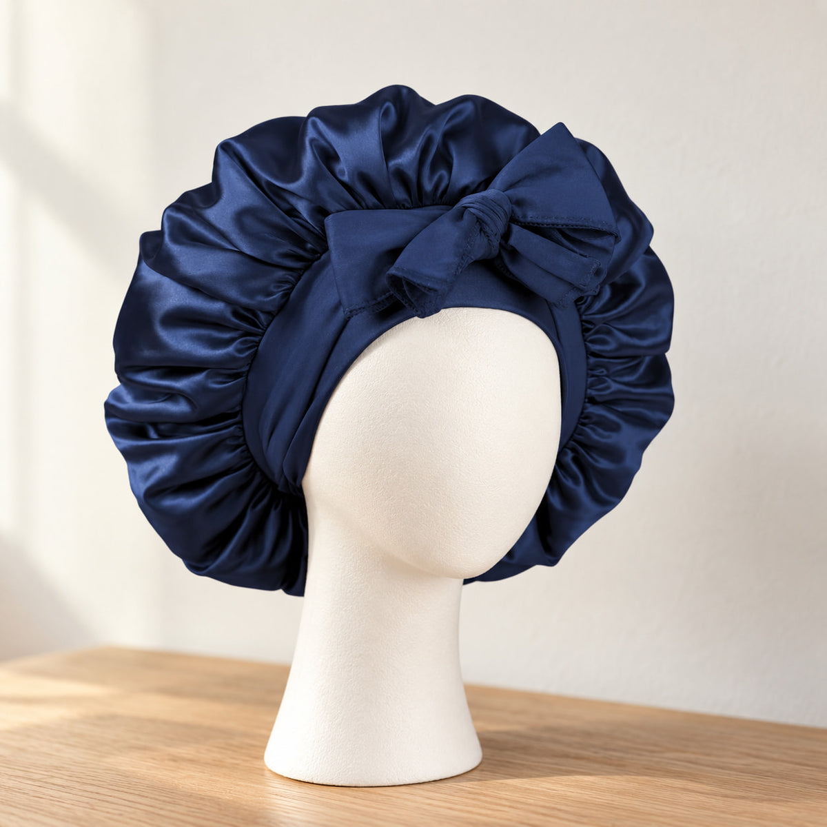 Bonnet de nuit en satin bleu nuit à nouer, présenté sur une tête de mannequin blanche