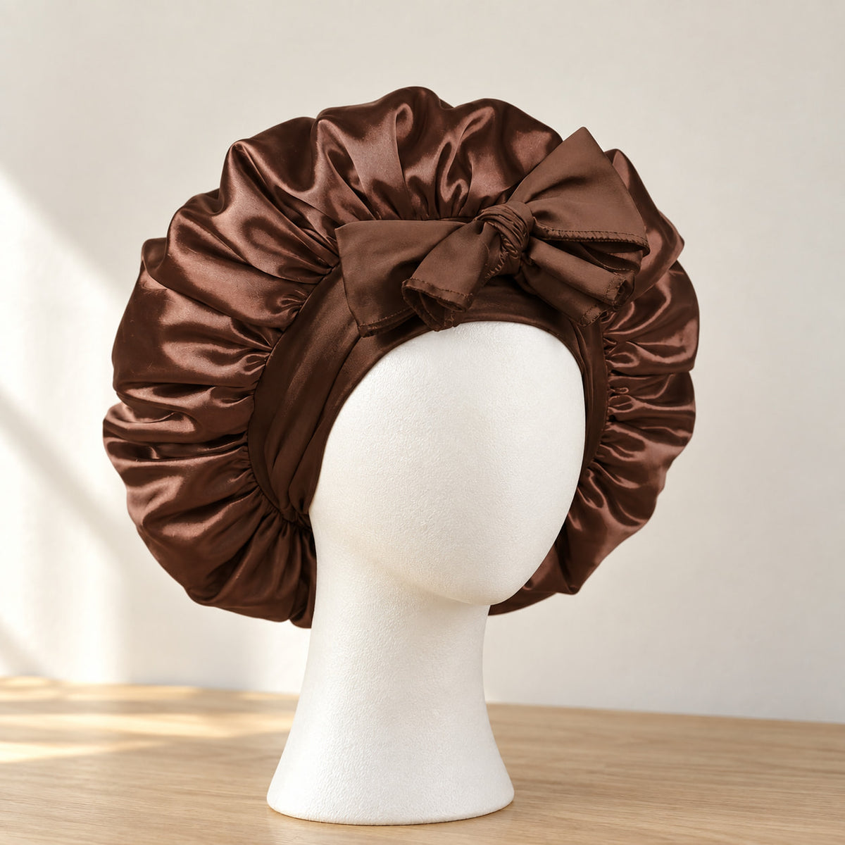 Bonnet de nuit en satin chocolat à nouer, présenté sur une tête de mannequin blanche