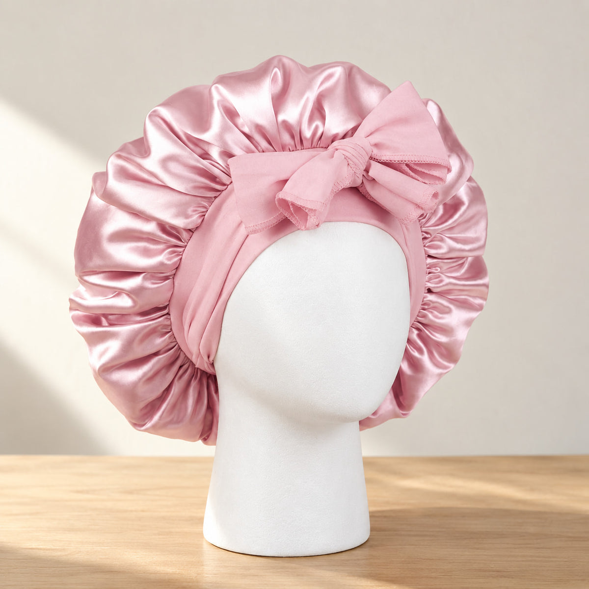 Bonnet de nuit en satin rose clair à nouer, présenté sur une tête de mannequin blanche