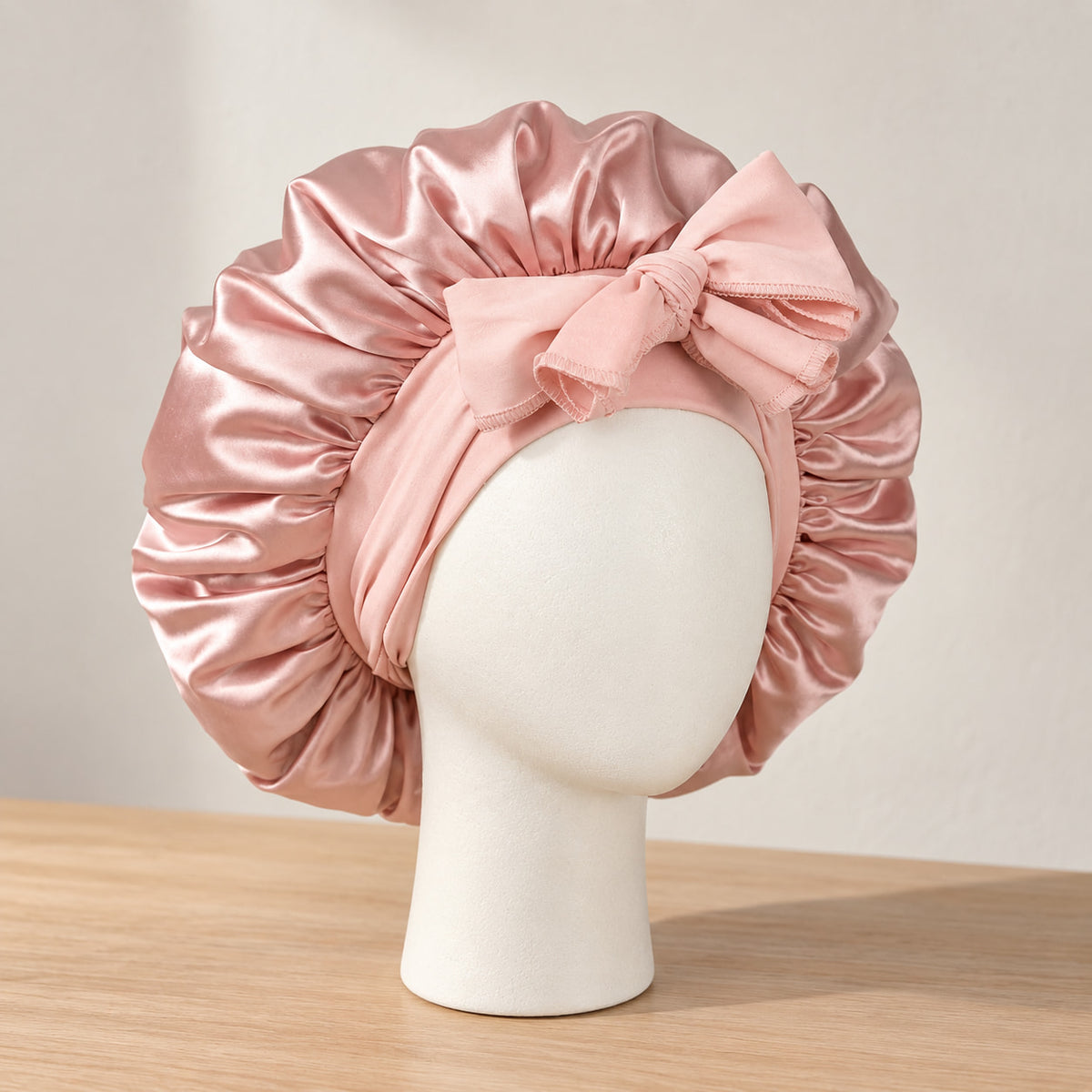 Bonnet de nuit en satin rose poudré à nouer, présenté sur une tête de mannequin blanche