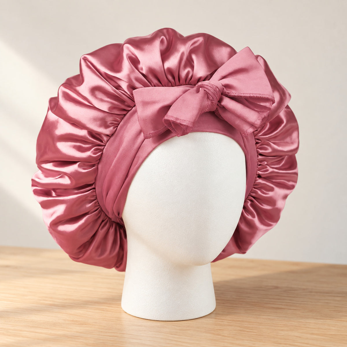 Bonnet de nuit en satin rose à nouer, présenté sur une tête de mannequin blanche